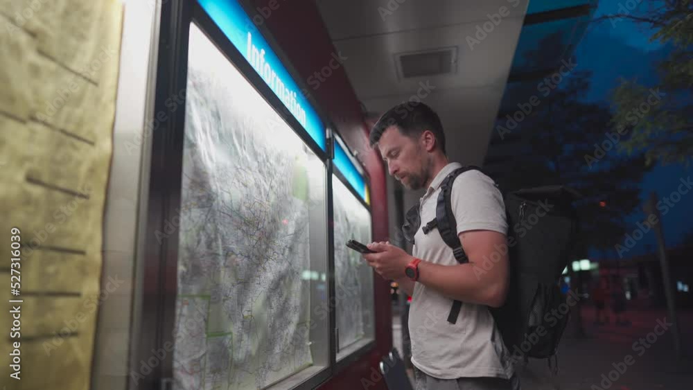 Thoughtful traveler using tourist transport map, looking for best way, transport connection standing at station in Germany, Munich. Man looking for location on mobile phone app and map board at stop Thoughtful traveler using tourist transport map, looking for best way, transport connection standing at station in Germany, Munich. Man looking for location on mobile phone app and map board at stop
