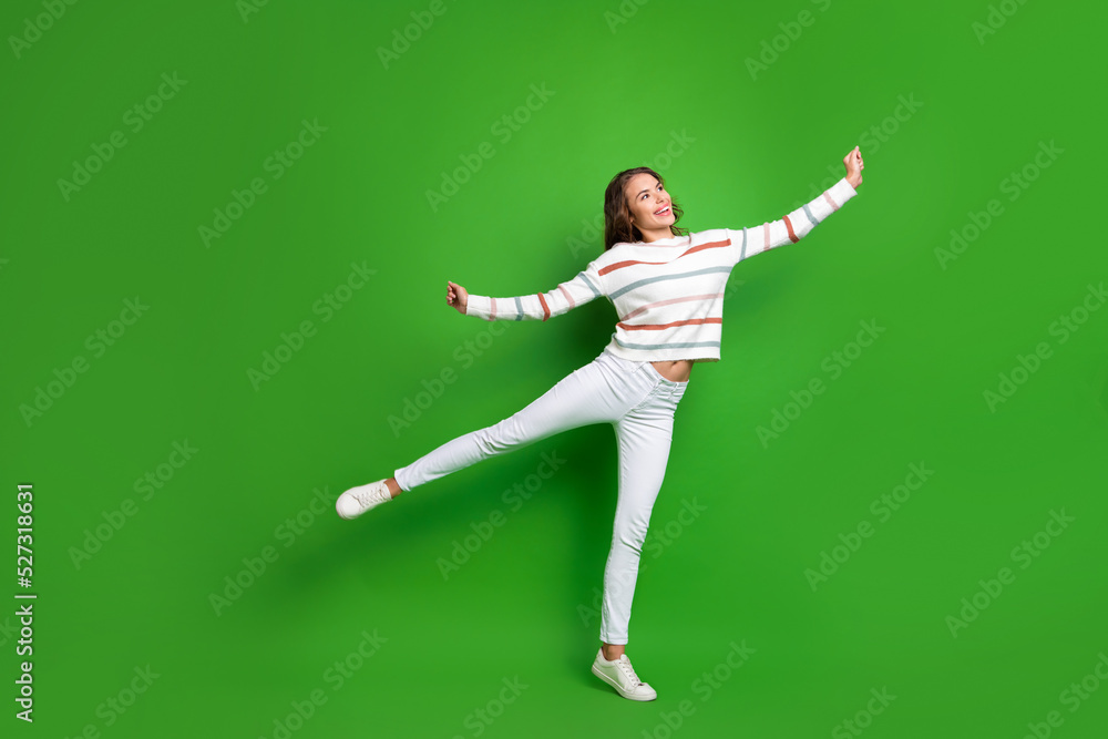 Full length photo of funny dreamy girl dressed striped pullover dancing looking empty space isolated green color background Full length photo of funny dreamy girl dressed striped pullover dancing looking empty space isolated green color background