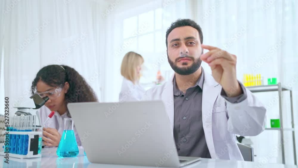 Scientist in lab coat and safety glasses holding glass plate at modern laboratory. Take note on the laptop for analysis. Research development, bio chemistry, medical, pharmaceutical Scientist in lab coat and safety glasses holding glass plate at modern laboratory. Take note on the laptop for analysis. Research development, bio chemistry, medical, pharmaceutical