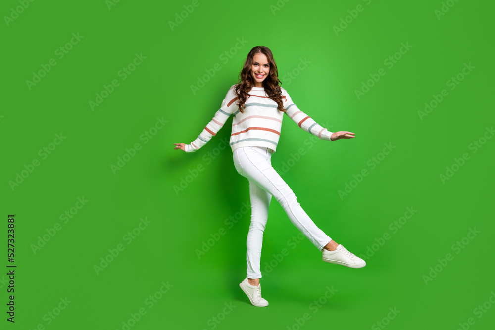 Full length photo of adorable shiny lady wear striped sweater walking dancing isolated green color background Full length photo of adorable shiny lady wear striped sweater walking dancing isolated green color background