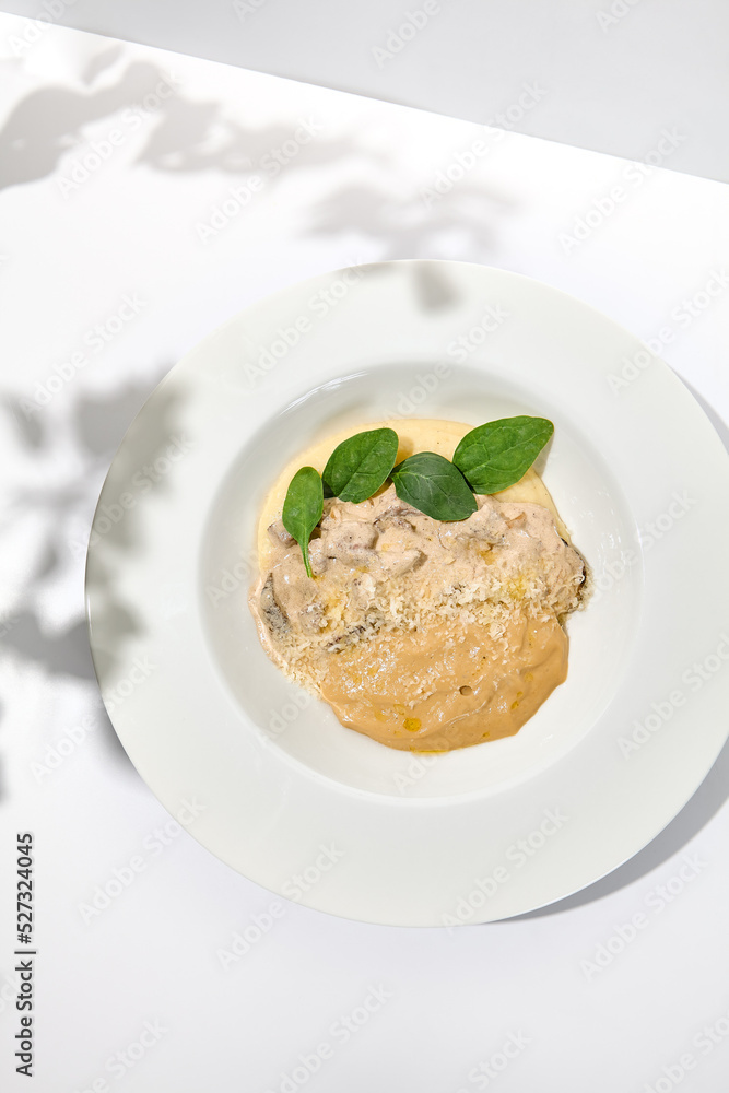 Traditional russian food - beef stroganoff with mushroom sauce and mashed potatoes. Beef stroganoff in white plate on light background with hard shadows. Stew meat with creamy sauce on summer menu.