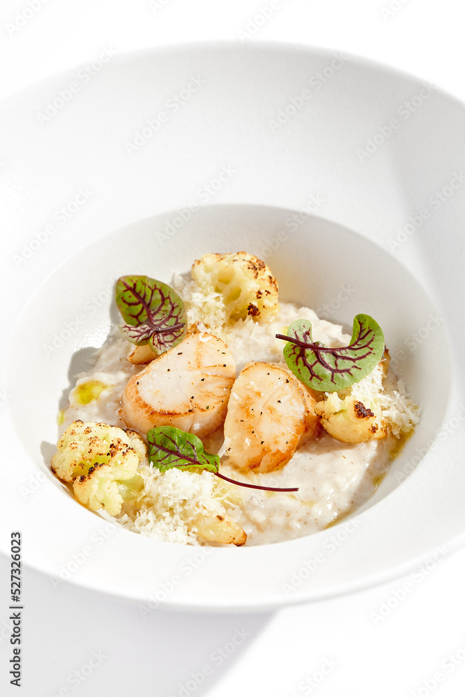 Delicious creamy risotto with sea scallop and cauliflower. Elegant main course with seafood on white plate. Grilled scallop with cauliflower and creamy rice. Seafood risotto with scallops Delicious creamy risotto with sea scallop and cauliflower. Elegant main course with seafood on white plate. Grilled scallop with cauliflower and creamy rice. Seafood risotto with scallops