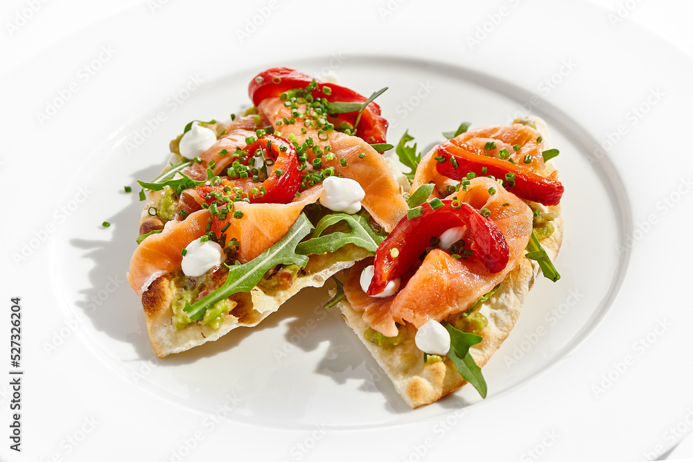 Bruschetta with salmon, avocado and paprika on white plate. Salmon bruschetta on crispy focaccia. Appetizer with guacamole, trout, cheese and paprika on toast. Fish antipasti in restaurant menu. Bruschetta with salmon, avocado and paprika on white plate. Salmon bruschetta on crispy focaccia. Appetizer with guacamole, trout, cheese and paprika on toast. Fish antipasti in restaurant menu.