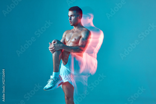 Youthful, athletic, pumped-up man does a warm-up. A man with a bare body and white shorts on a blue background. © Georgii