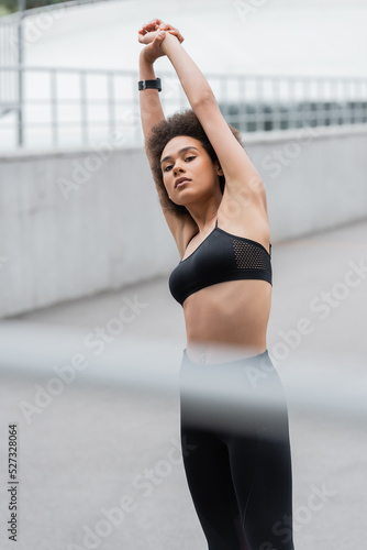 African american sportswoman warming up and looking at camera on stadium.