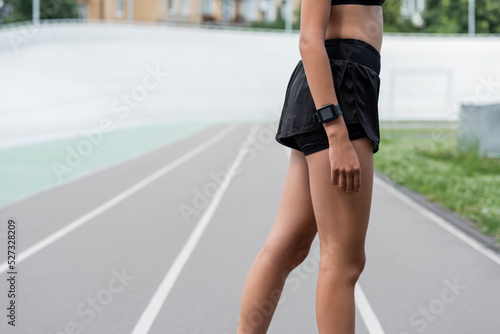Cropped view of african american sportswoman with smart watch standing on stadium.