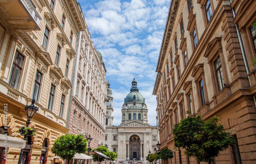 Old town street buildings and the St. Stephen's Basilica, a Roman Catholic Cathedral in the old town of Budapest, Hungary, Europe. Church tower among historical houses. Urban downtown neighborhood.