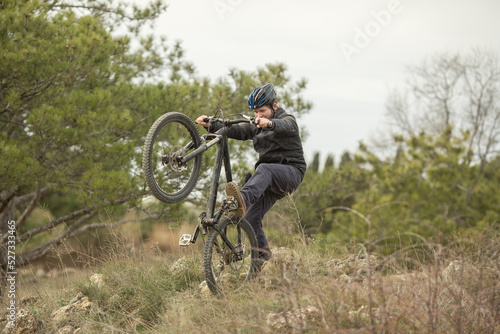 a young man in a bicycle helmet rides down the mountain on a mountain bike. He rides on the back wheel and falls