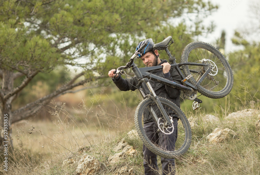 a young man in a bicycle helmet carries a bicycle from the mountain. a young man in a bicycle helmet carries a bicycle from the mountain.