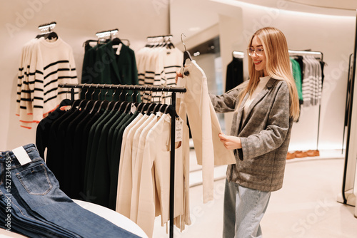 A smiling young shopaholic woman tries on clothes in a shopping mall store, walks through boutiques. Consumerism is a modern problem of society. Anti-environmental