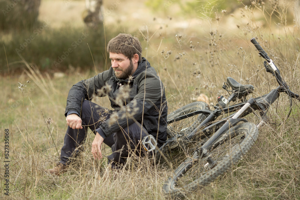 a young man is sitting in a clearing in the forest next to a mountain bike