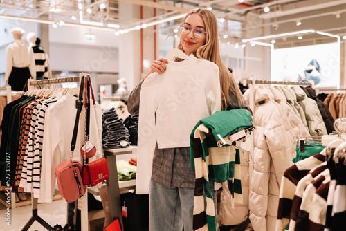 A smiling young shopaholic woman tries on clothes in a shopping mall store, walks through boutiques. Consumerism is a modern problem of society. Anti-environmental photo