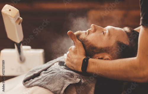 Fototapeta Barber hairdresser steams skin of man face before dangerous shave with razor