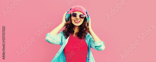 Colorful portrait of happy smiling young woman listening to music in headphones wearing casual hat on pink background © rohappy
