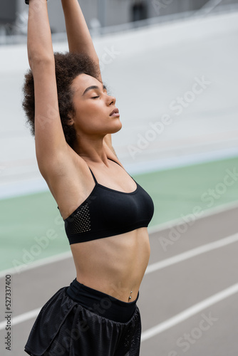 Fit african american sportswoman stretching with closed eyes on stadium.