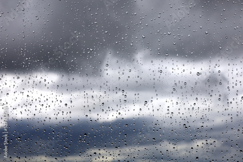 Raindrops on window glass on blurred background of sky with storm clouds. Beautiful water drops, rainy weather