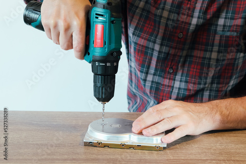 Drilling a Hard Disk Drive to Destroy Evidence Data close up.Cropped image of hand drilling on hard drive at table photo