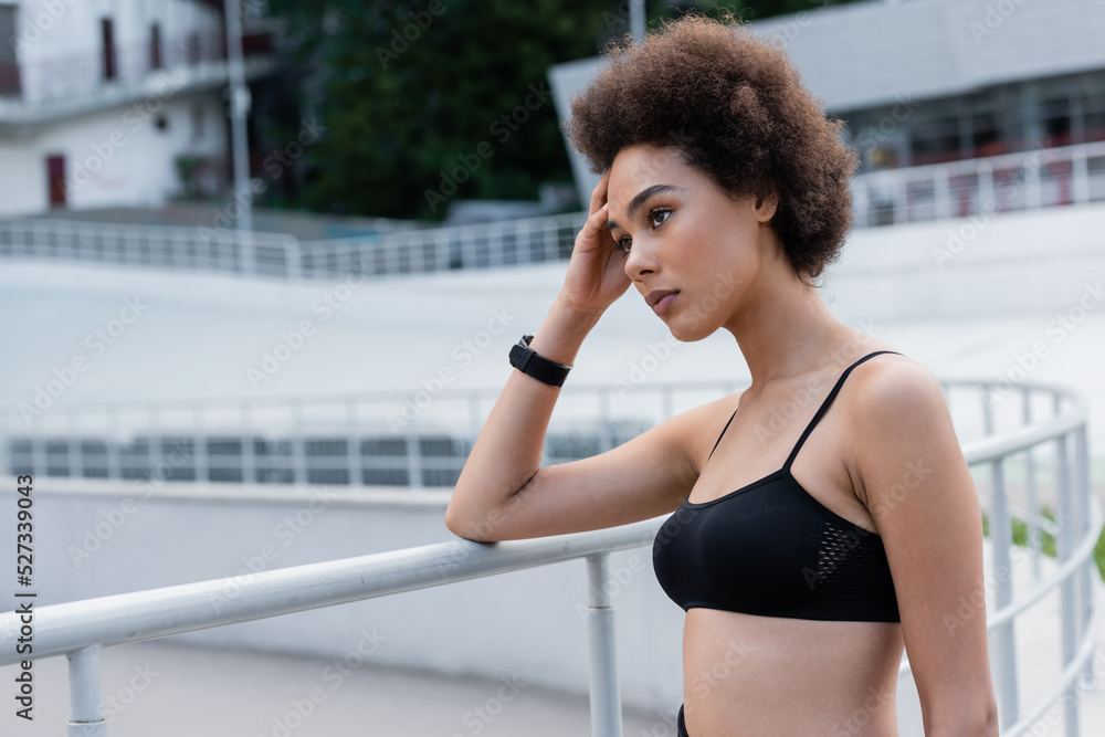 pensive african american sportswoman holding hand near head and looking away outdoors. pensive african american sportswoman holding hand near head and looking away outdoors.