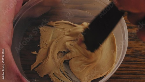 A man spreads putty in a jar, stirring with a spatula. Medium plan photo