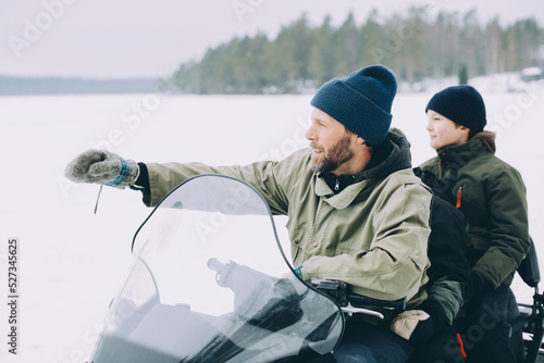 Mature man gesturing while snowmobiling with boys photo