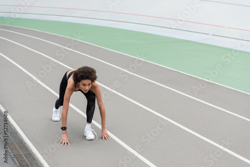 young african american woman in white sneakers standing in low start pose on track.