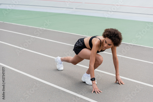 slim african american runner looking away while standing in low start pose.