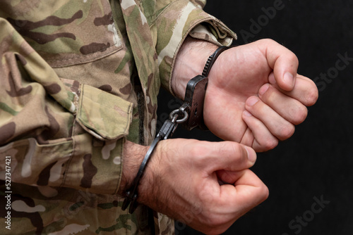 A soldier in a military camouflage uniform is handcuffed on a black background.