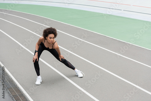 young african american woman warming up on stadium while doing side lunge exercise.