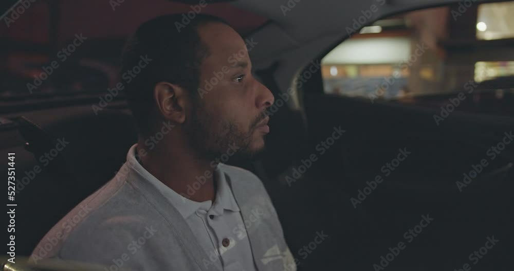 A black man seated in car backseat commuting from work at night. African American person riding taxi cab in the evening A black man seated in car backseat commuting from work at night. African American person riding taxi cab in the evening