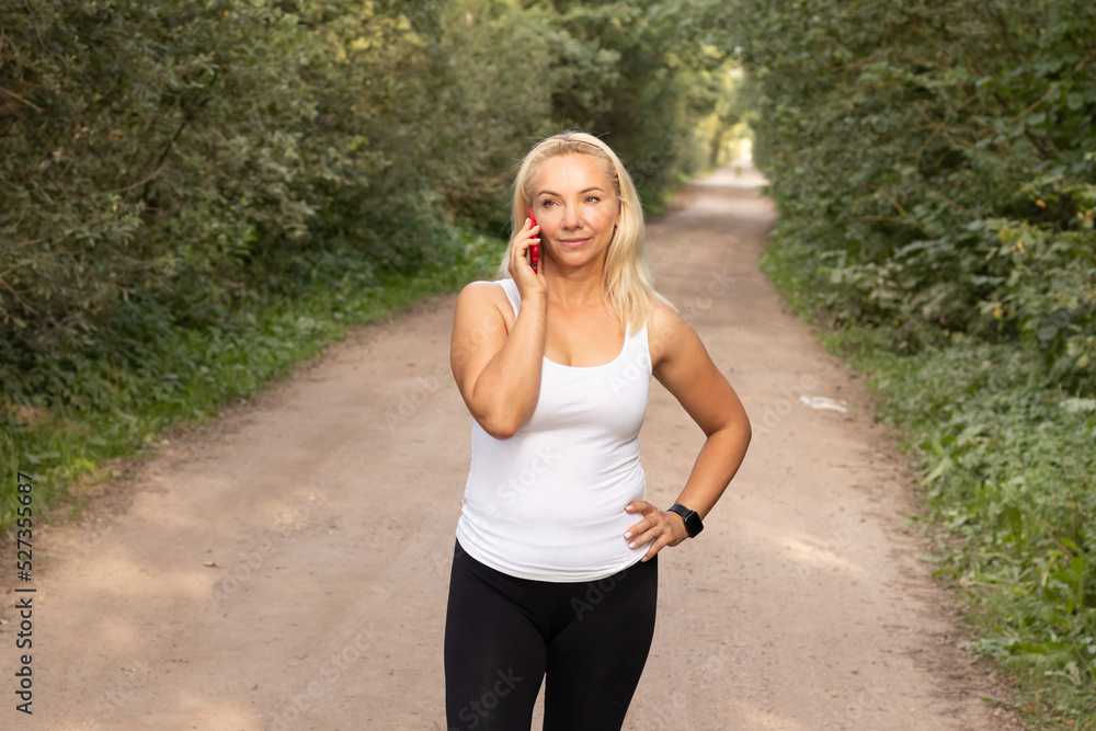 a young beautiful girl talking on the phone before jogging through the woods on a hot summer day Healthy lifestyle a young beautiful girl talking on the phone before jogging through the woods on a hot summer day Healthy lifestyle