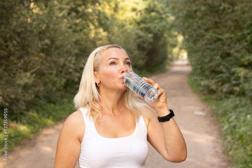 a young beautiful girl drinks water from a bottle while jogging through the forest on a hot summer day Healthy lifestyle a young beautiful girl drinks water from a bottle while jogging through the forest on a hot summer day Healthy lifestyle