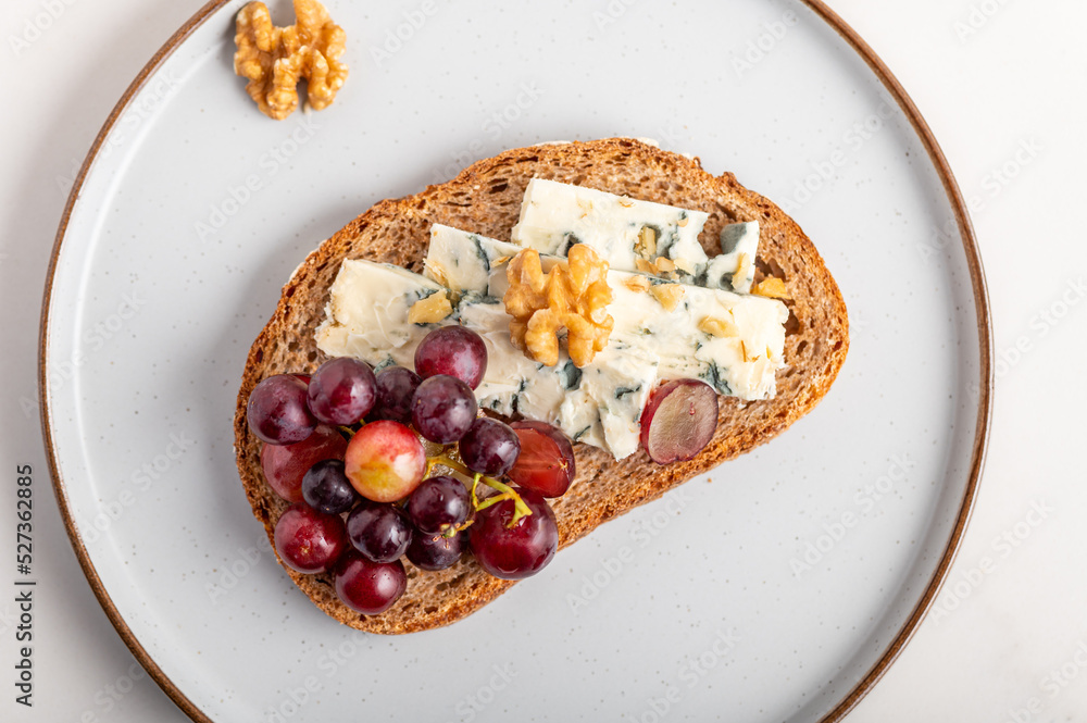 Toasted bread with mild creamy blue cheese, grapes and walnuts on grey plate Toasted bread with mild creamy blue cheese, grapes and walnuts on grey plate