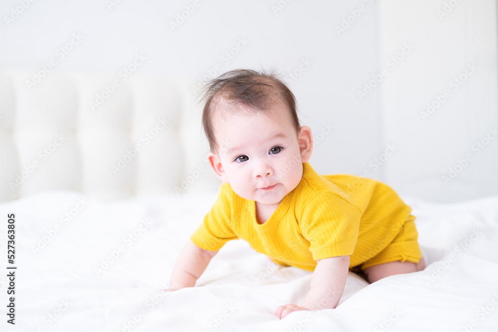 healthy asian baby girl 5 months in yellow bodysuit on bed on white bedding