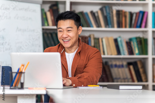 Cheerful Asian Tutor Man Using Laptop Teaching Online At Workplace