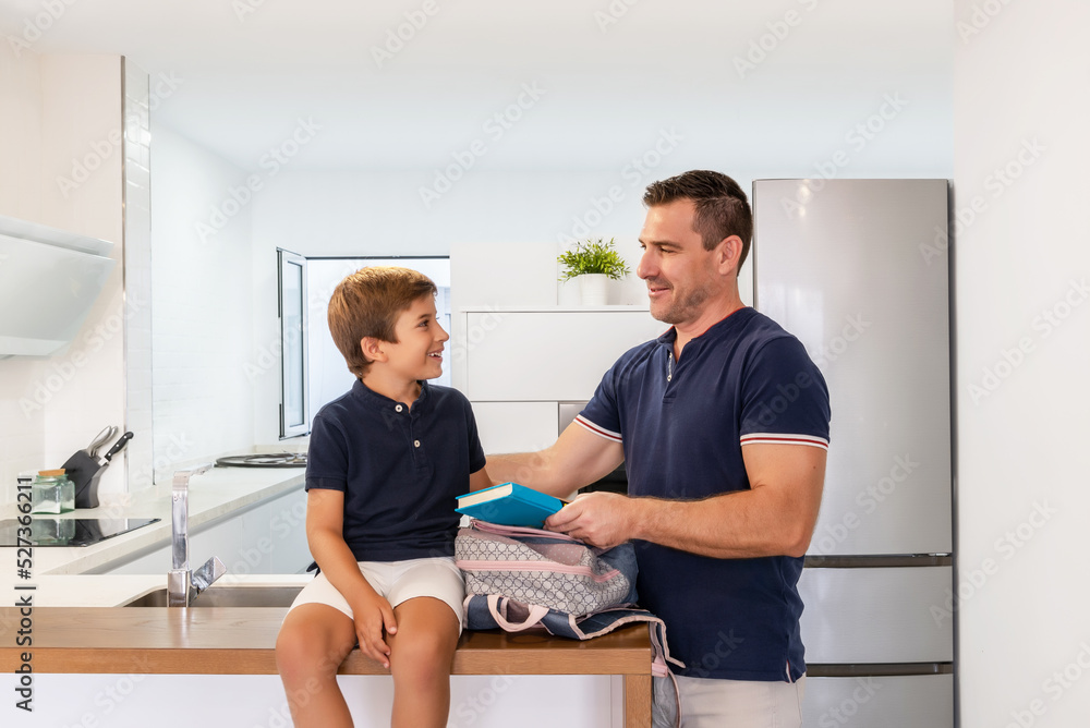 Single father preparing his son's backpack before going to school. Single parent family. First day of school. Child happy to go back to school Single father preparing his son's backpack before going to school. Single parent family. First day of school. Child happy to go back to school