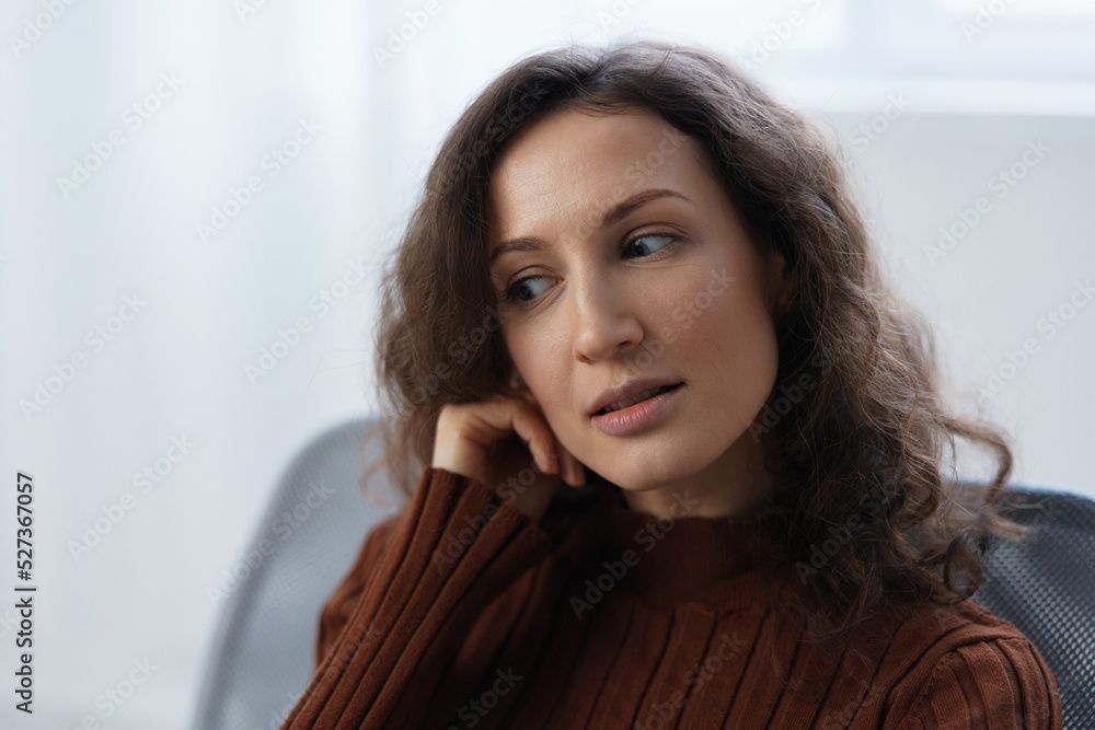 Pensive focused frustrated curly pretty woman lost in sad thoughts about irreparable mistake decision about divorce sit in chair at home looks aside. Depression Heavy thoughts concept. Closeup shot Pensive focused frustrated curly pretty woman lost in sad thoughts about irreparable mistake decision about divorce sit in chair at home looks aside. Depression Heavy thoughts concept. Closeup shot