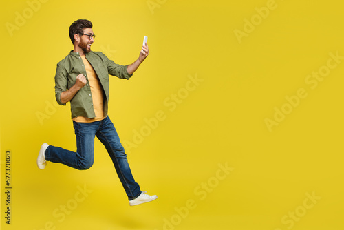 Full length shot of excited man looking at smartphone and making YES gesture, jumping in excitement, copy space