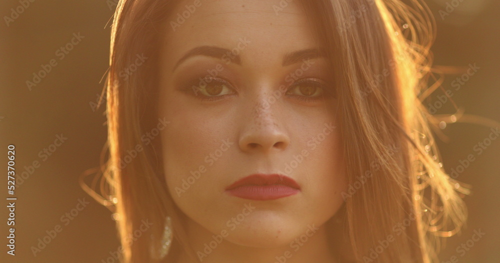 Young woman face looking to camera during glow orange sunset light outdoors Young woman face looking to camera during glow orange sunset light outdoors