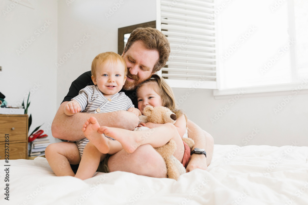 Father embracing son (12-17 months) and daughter (2-3) on bed Father embracing son (12-17 months) and daughter (2-3) on bed