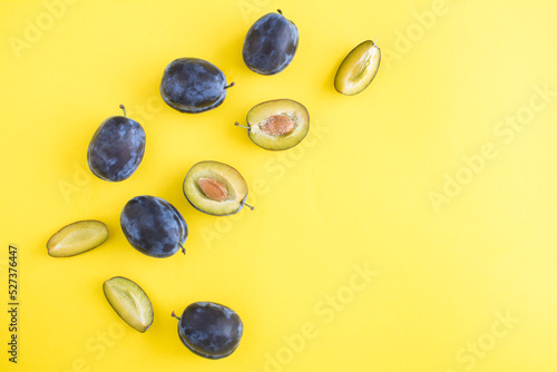 Ripe whole and cut blue plums on the yellow background.Top view. Copy space.