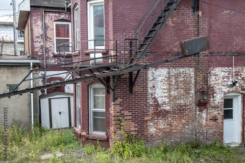 Exterior of abandoned run down two storey red brick house with large steel fire escape in a weedy lot, daytime, nobody photo