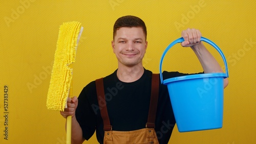 A young man in uniform holds a bucket of water and a mop in his hands. Janitor cleans and disinfects the space