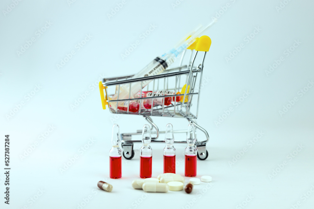 Medical ampoules with red medicine. A shopping cart with pills and syringes. Selective focus.