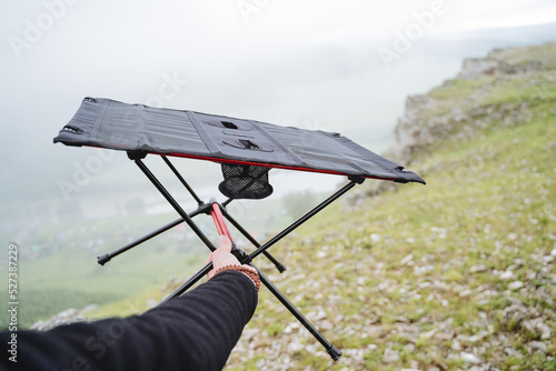 Compact folding table for camping in nature, camping equipment dining table, hand holds the frame of the table.