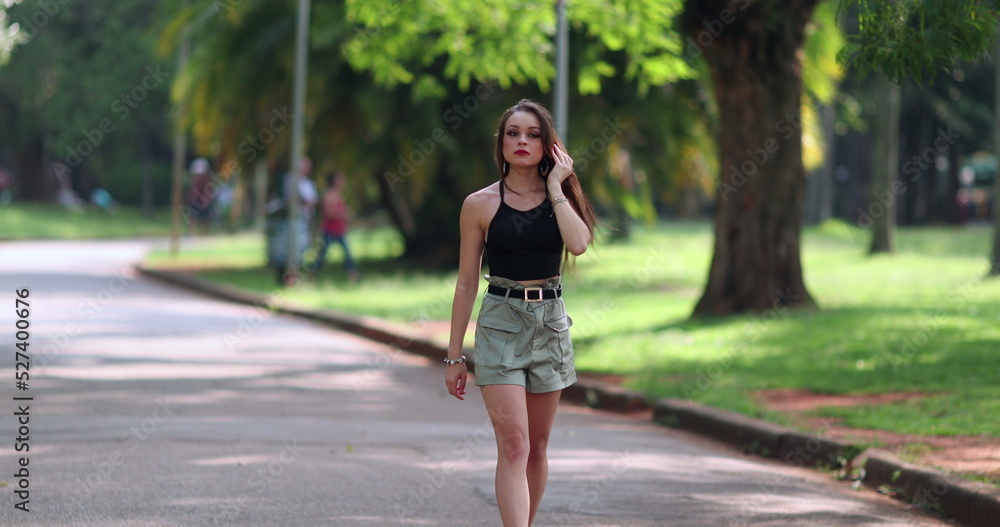 Young woman walking outside at park. Pretty millennial girl leisure walk outdoors enjoying sunlight