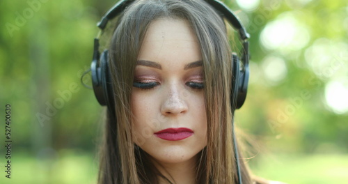 Young woman wearing headphones and holding smartphone device. Pretty girl listening to music, song, or podcast outdoors