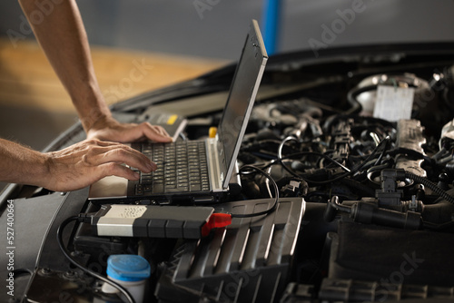 Auto mechanic uses laptop while conducting diagnostics test. Modern car service. Computer diagnostics of the car. European car mechanic holds a digital device photo