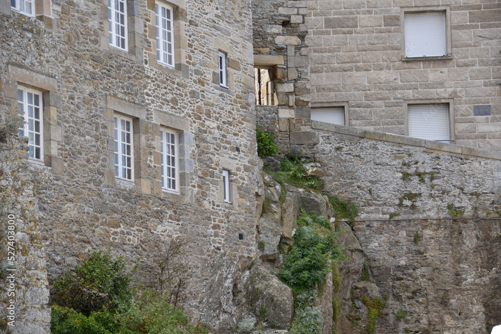 Fototapeta premium Historic stone buildings with multiple windows, situated on a rocky slope, showcasing detailed masonry and a natural environment. The scene exudes a rustic and timeless charm.