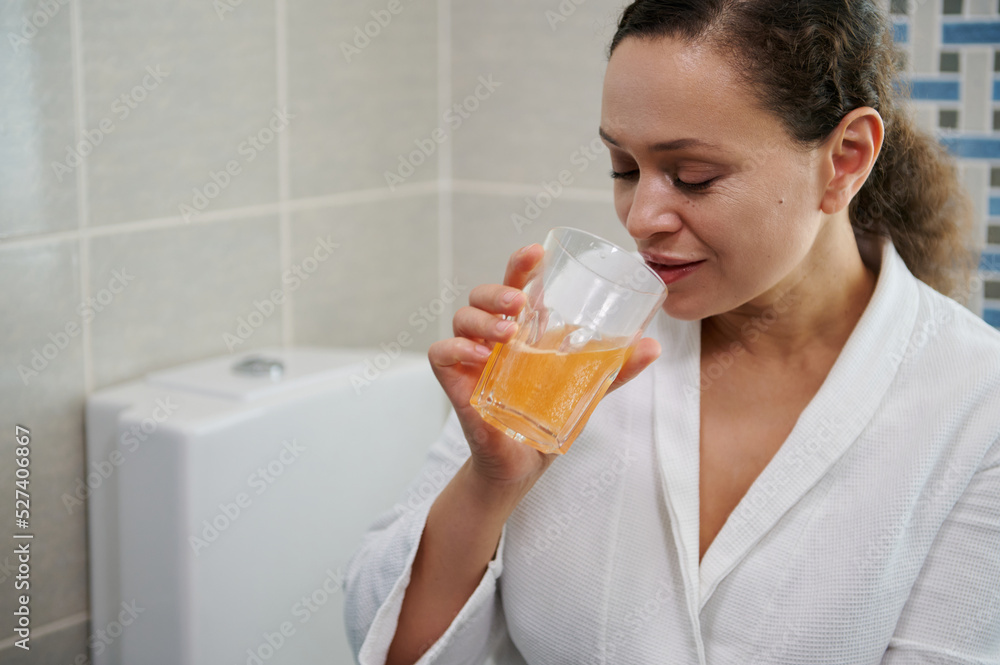 Multi-ethnic pretty woman in white bathrobe, drinking water with effervescent painkiller pills, according to physician's prescription. Woman suffering head ache. Migraine and fever, pain relievers. Multi-ethnic pretty woman in white bathrobe, drinking water with effervescent painkiller pills, according to physician's prescription. Woman suffering head ache. Migraine and fever, pain relievers.