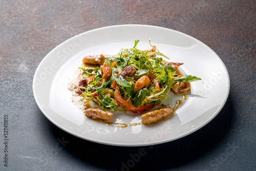 Salad with seafood on white plate on dark stone table